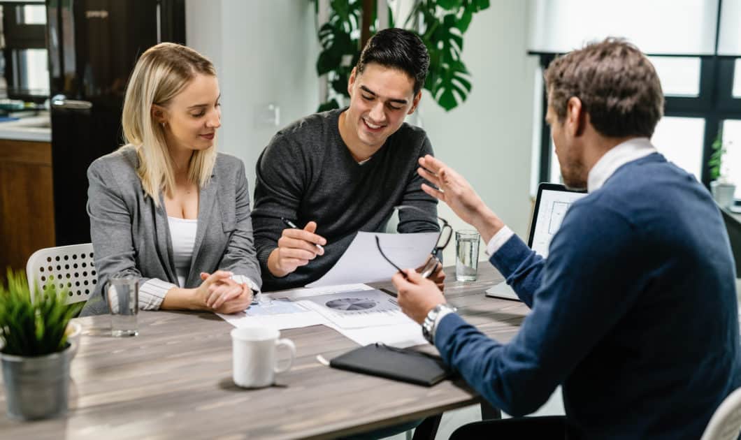 Happy Couple Going Through Paperwork While Having Meeting With Financial Advisor.